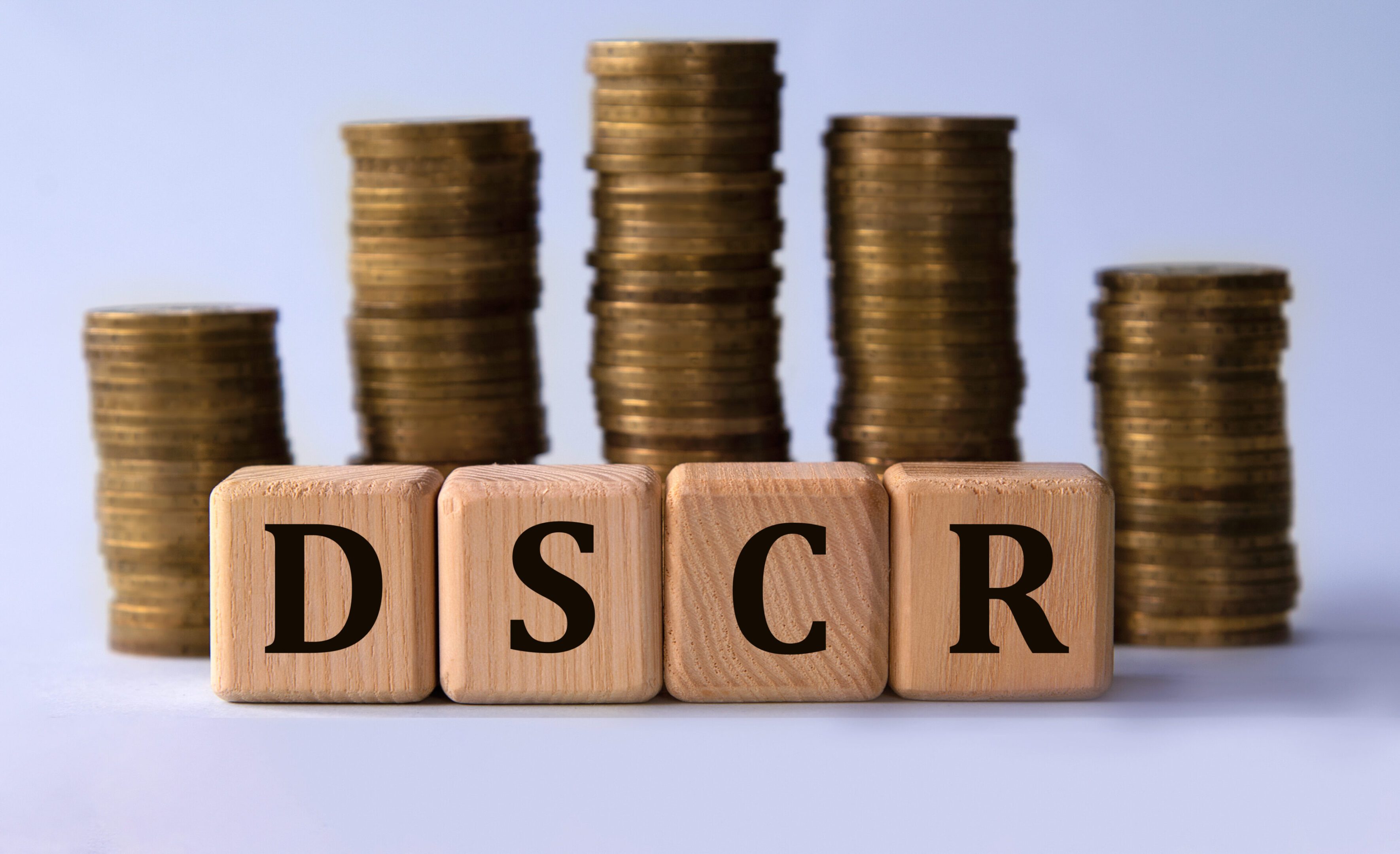 DSCR (Debt Service Coverage Ratio) - acronym on wooden cubes on the background of stacks of coins. Business concept